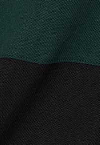 Gros plan d'un tissu tricoté texturé vert foncé et noir avec une couture nette entre les deux couleurs.