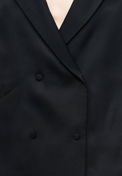 Μαύρο διπλό στήθος σακάκι με κομψό σχέδιο, διαθέτοντας βαθύ V-λαιμό, ομαλή υφή και δύο κουμπιά καλυμμένα με ύφασμα.