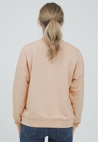 Ferskenfarget sweatshirt med avslappet passform, senket skuldre, ribbede mansjetter og kant. Myk tekstur, uten synlige mønstre eller detaljer.