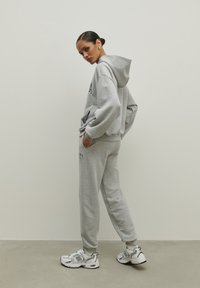 Szary sweatshirt z kapturem i kieszenią z przodu, zestawiony z pasującymi spodniami dresowymi. Posiada elastyczne mankiety oraz sneakersy z jasnymi akcentami.