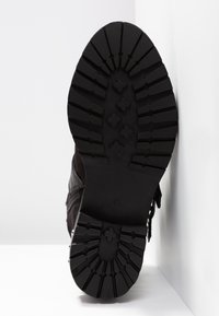 Suela de zapatilla negra con un patrón de goma texturizada, formas hexagonales y en cruz, con una etiqueta de tamaño visible '37' en la parte inferior.