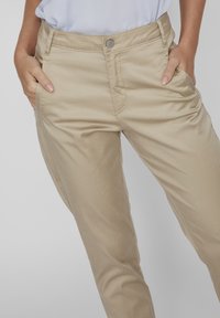 Pantaloni in cotone beige con una texture liscia, dotati di tasche anteriori e chiusura con bottone in vita. Design casual con vestibilità a gamba dritta.
