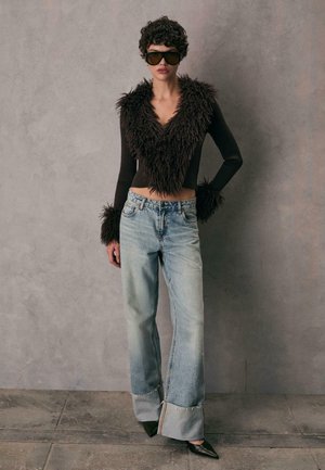 Maglione corto shaggy marrone con maniche lunghe, abbinato a jeans baggy azzurri chiari con orlo sfrangiato e tacchi neri a punta.