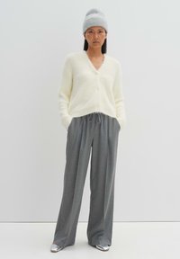 Cardigan fluffy crema con scollo a V e chiusura con bottoni, abbinato a pantaloni grigi con coulisse e scarpe slip-on argento. Cappello beanie grigio.