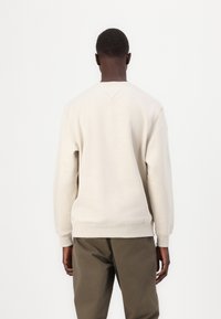 Lys beige sweatshirt laget av bomullsblanding, med rund hals, ribbede mansjetter og en avslappet passform, kombinert med olivengrønne bukser.