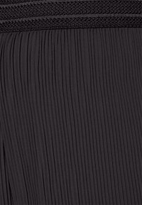 Schwarzer, plissierter Stoff mit einem strukturierten Taillenbund. Die Falten verlaufen vertikal und verleihen eine weiche Optik und einen subtilen Glanz.