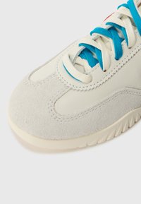 Adidași cu un superior din piele albă cremoasă, cu accente din suede gri, șireturi turcoaz și o talpă din cauciuc texturat pentru aderență.