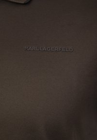 Brązowa koszulka polo z teksturowanej tkaniny, z wytłoczonym logiem "KARL LAGERFELD" w tym samym kolorze na klatce piersiowej. Klasyczny krój kołnierza.