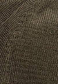 Tissu en velours côtelé marron avec des nervures verticales, présentant une texture lisse et un petit bouton sombre en détail sur la surface.