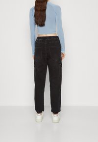 Modrý dlouhý rukáv crop top zkombinovaný s černými cargo kalhotami. Cargo kalhoty mají boční kapsy a celý outfit doplňují bílé tenisky.