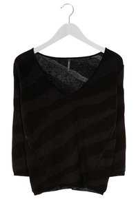 Svart V-ringad tröja med en lös passform, som har ett texturerat vågmönster och ett något genomskinligt, stickat tyg. Hänger från en vit krok.