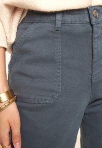 Pantalones de mezcla de algodón gris con una textura suave, que presentan bolsillos frontales en ángulo y un cierre de botón. Acentuados con detalles de costura.