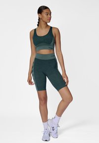 Komplet sportowy składający się z stanika i szortów w ciemnozielonym kolorze. Tkanina o fakturze z kontrastującymi szarymi akcentami. Posiada pas środkowej wysokości i dopasowany krój.