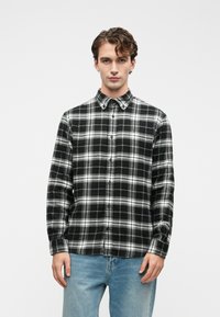 Camisa de botão preta e branca em padrão xadrez, com colarinho clássico e mangas compridas, combinada com jeans de ganga azul clara.