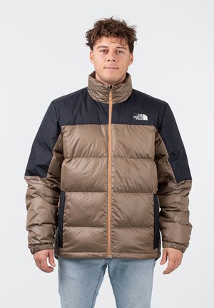 Gevoerde jas in bruin en marineblauw, met een horizontaal quiltontwerp, hoge kraag en ritsluiting. Het logo van The North Face staat op de borst.