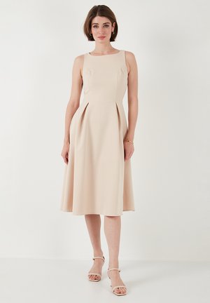 Knee-length, sleeveless dress in soft beige fabric with fitted bodice, pleated skirt, and round neckline. Minimalist design with smooth texture.