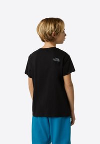 Fekete pamut póló rövid ujjakkal, középen hátul egy kis szürke logóval. A modellen kék melegítőnadrág van.