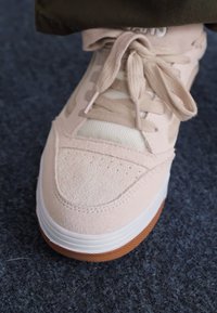 Light pink sneaker with suede upper, mesh panels, and white sole. Features textured toe cap and flat laces. Designed for casual wear.
