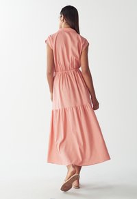 Różowa maxi sukienka z krótkimi rękawami, elastycznym pasem i warstwowym dołem; wykonana z miękkiego materiału o gładkiej fakturze.