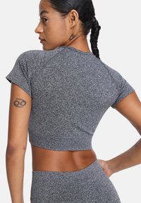 Top atlético gris recortado con mangas cortas, que cuenta con una tela texturizada y costuras en contraste. Incluye un tatuaje visible en el brazo.