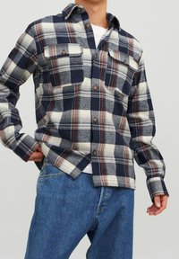 Marinblå och krämrandig flanellskjorta med bruna knappar, långa ärmar, två bröstfickor och rak nederkant, bärs över blå jeans.