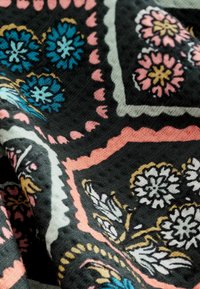 Textil multicolor cu modele florale în albastru, roz și alb pe un fundal negru. Împletitură moale, texturată, cu margini geometrice.