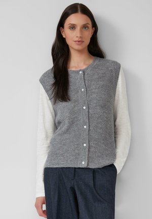 Cardigan en tricot gris avec un motif texturé, doté d'un col rond et d'une fermeture à boutons, associé à une chemise à manches longues de couleur claire.