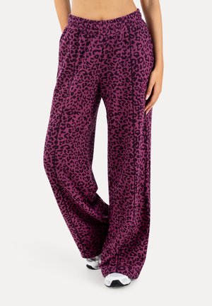 Lilla bukser med brede ben og sort leopardmønster, båret med hvide sneakers, vist fra talje til fødder mod hvid baggrund.