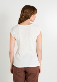 Top blanco de manga corta con escote redondeado y corte holgado. Confeccionado en una tela ligera y texturizada, presenta un dobladillo curvado.