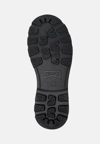 Suela de zapato de goma negra con patrón texturizado y surcos pronunciados. Presenta la marca "CAMper" y la inscripción "BRIDGE XTRAGRIP" en relieve sobre la superficie.