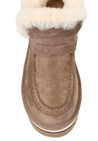 Brązowy zamszowy botek za kostkę z puszystym kołnierzem z kremowej owczej skóry. Ozdobne szwy i okrągły przód. Płaska podeszwa z białym paskiem.