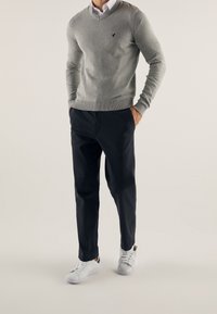 Szary sweter w serek, dopasowany krój, granatowe spodnie i białe sneakersy. Sweter ma prążkowane mankiety i dół; małe logo na piersi.