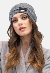 Beanie a motivo houndstooth grigio con un accento in velour nero, realizzato in un tessuto morbido, che presenta una vestibilità aderente e una texture liscia.