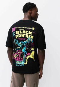 Must t-särk, millel on koomiksistiilis graafika Mustast Pantrist erksates värvides (kollane, roosa, sinine) ning julgete tekstide ja tegevusdetailidega.
