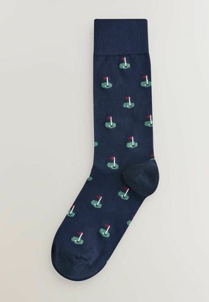 Chaussettes navy avec un motif répété de trous de golf avec des drapeaux et de l'herbe verte. Fabriquées à partir d'un matériau textile doux, avec une texture lisse.