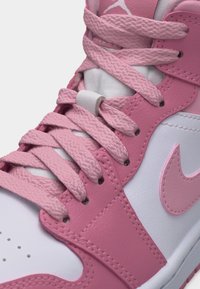 Približen posnetek roza in belih superg z teksturiranimi roza vezalkami in našitkom Nike Swoosh na bočni strani.