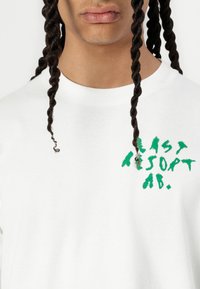 White cotton sweatshirt featuring green embroidered text "EASY RESORT AB." Classic crew neck design with a smooth texture.