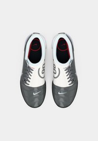 Ténis de desporto cinzas e brancos com um upper liso, biqueira cinza texturizada, atacadores cinzas e logótipo da Nike na lateral e na palmilha.