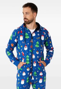 Mono azul con cremallera, hecho de tela suave y con motivos navideños como Papá Noel, árboles y copos de nieve. Tiene capucha y dos bolsillos frontales.