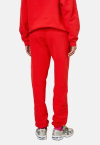 Sarkans džemperis un atbilstošas sporta bikses, kas izgatavotas no mīksta, teksturēta auduma. Iezīmēta ar brīvu piegriezumu un ribotiem maliņām. Saskaņots ar sudraba sporta apaviem.