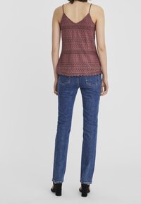 Débardeur en dentelle bordeaux avec bretelles spaghetti, présentant des motifs complexes et un ourlet festonné ; associé à un jean skinny en denim bleu.