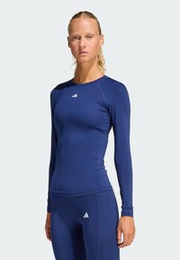 Navy long-sleeve athletic top made of stretchy fabric, featuring a round neck, fitted design, and white logo on the chest.