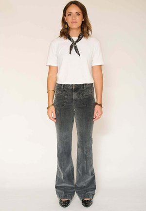 Tenue féminine composée d'un t-shirt en coton blanc, de pantalons en velours côtelé gris à évasement et de chaussures à talons noires avec des accents cloutés.