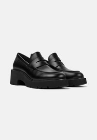 Par de mocasines de piel negra con plataforma y suelas gruesas, con un diseño clásico de tira de centavo sobre un fondo blanco.