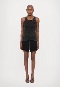 Svart tank topp med teksturert finish, kombinert med et svart miniskjørt med glidelås foran og buet kant. Stroppe-sandaler i svart.