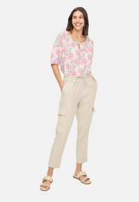 Bluse mit floralem Muster und kurzen Ärmeln in hellrosa und grau. Beigefarbene Cargo-Hose mit Seitentaschen und elastischem Bund. Braune Pantoletten.