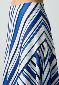 Une jupe rayée bleu et blanche avec une texture à côtes verticales et un design évasé, présentant des rayures de différentes largeurs dans des teintes sombres et claires.