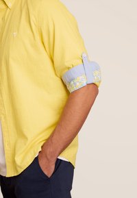 Geel overhemdd blouse met opgerolde mouwen, voorzien van lichtblauwe accenten en een bloemenpatroon op de binnenmanchet. Relaxed fit en lichtgewicht stof.