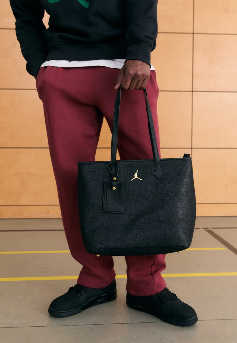 Juoda rankinė su tekstūruotu raštu, auksinėmis detalėmis ir dviem rankenomis. Derinama su bordo spalvos sportinėmis kelnėmis ir juodais sportbačiais.