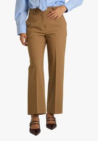 Pantaloni su misura color beige con design a gamba dritta, texture liscia e tasche laterali. Abbinati a ballerine appuntite in pelle verniciata scura.